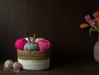 Koyu kahverengi ahşap arka planda, ahşap bir sepetin içindeki ahşap kancalı renkli yün toplar.