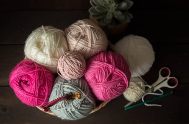 Koyu kahverengi ahşap arka planda, ahşap bir sepetin içindeki ahşap kancalı renkli yün toplar.