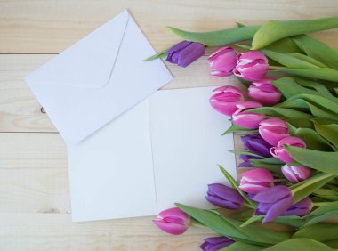 Beyaz kart ve zarf ahşap zemin üzerinde metin modellemesi için yeri olan laleler.