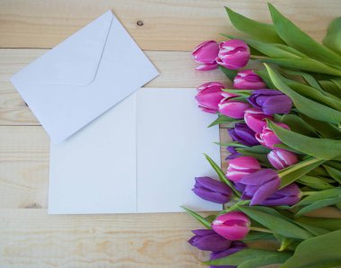 Beyaz kart ve zarf ahşap zemin üzerinde metin modellemesi için yeri olan laleler.