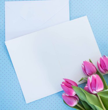 Beyaz kart ve zarf mavi zemin üzerinde metin modelleme için yeri olan laleler