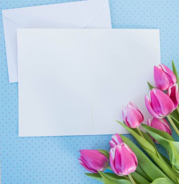 Beyaz kart ve zarf mavi zemin üzerinde metin modelleme için yeri olan laleler
