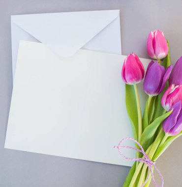 Gri zemin üzerinde beyaz kart ve zarf ve metin modelleme için yeri olan laleler.