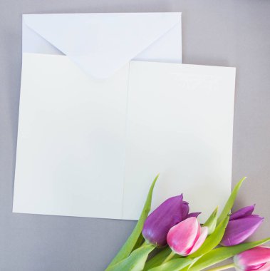 Gri zemin üzerinde beyaz kart ve zarf ve metin modelleme için yeri olan laleler.
