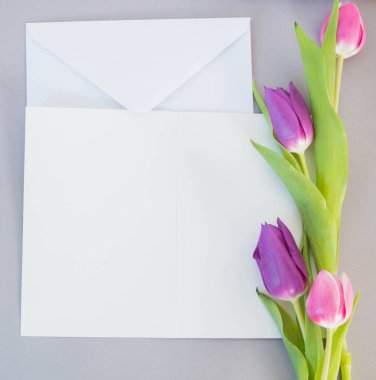 Gri zemin üzerinde beyaz kart ve zarf ve metin modelleme için yeri olan laleler.