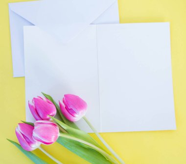 Beyaz kart ve zarf sarı zemin üzerinde pembe laleler ve metin için yer.