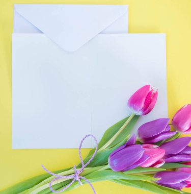 Beyaz kart ve zarf sarı zemin üzerinde pembe laleler ve metin için yer.