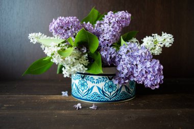 Koyu kahverengi ahşap arka planı olan mavi desenli bir kutuda beyaz ve mor liyak.