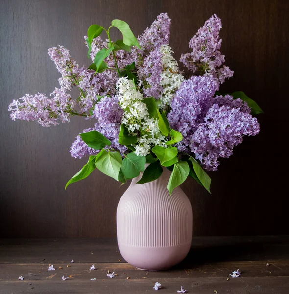 white and purple lilac in vase in front of a dark brown wooden wall spring
