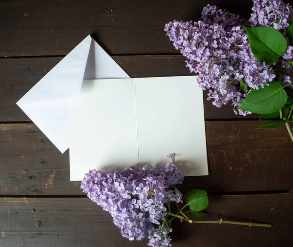 Koyu kahverengi ahşap zeminde mor leylak çiçeği ve yazı için yeri olan beyaz kağıt.