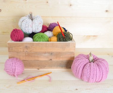 Beyaz kumaş sepetinde renkli yün toplar ve ahşap zemin üzerine kancalar.