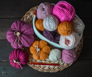 Örgü kancalı beyaz kumaş sepetinde renkli balkabakları sonbahar yaprakları ve yün toplar arka planda.