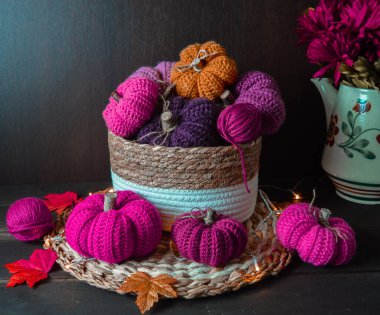 Koyu kahverengi ahşap zemin üzerinde sonbahar yaprakları olan pembe renkli örgü balkabakları. Örgü kancası ve yün toplar arka plandan düşüyor.