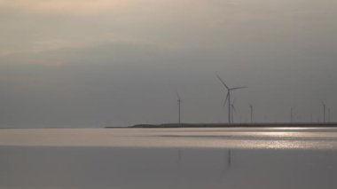 Gölün kıyısında rüzgar türbinleri var. Akşam vakti. Yeşil enerji kavramı