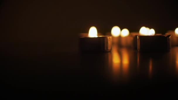 Закройте маленькие свечи в алюминиевых подсвечниках на столе в темноте. — стоковое видео