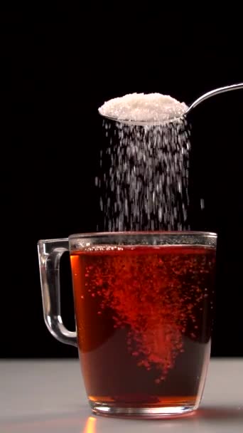 Белый сахар падает в чашку чая в замедленной съемке на черном фоне — стоковое видео
