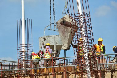 SELANGOR, MALAYSIA 12 Aralık 2015: İnşaat alanındaki kereste formuna beton kova kullanarak ıslak beton döken bir grup inşaat işçisi.  