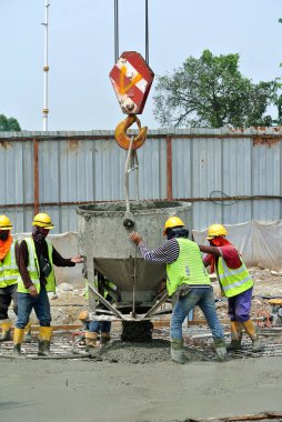 SELANGOR, MALAYSIA 12 Aralık 2015: İnşaat alanındaki kereste formuna beton kova kullanarak ıslak beton döken bir grup inşaat işçisi.  