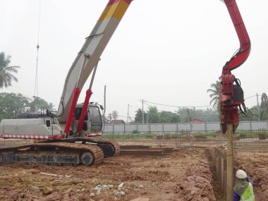 SELANGOR, MALAYSIA 25 Mart 2015: inşaat alanında çarşaf yığını cofferdam sürücü makine. Makine titreşimli hidrolik kolu kullanarak çarşaf yığınını yere itti. İşçi kontrolü. 