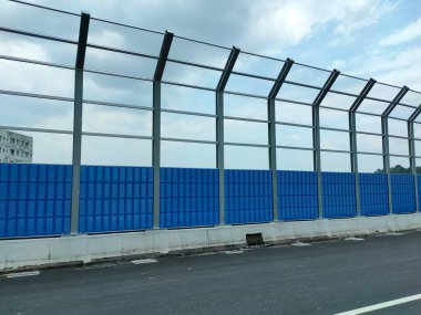 SELANGOR, MALAYSIA - JULY 5, 2020: Noise barriers are installed along the vehicle lane bordering the residence to prevent noise pollution to the surrounding locals. clipart