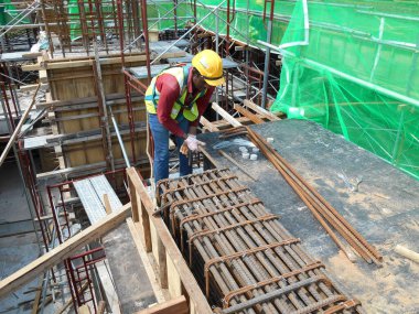 MALACCA, MALAYSIA - 30 Mart 2016: Malezya 'nın Malacca kentindeki inşaat alanında çelik takviye barı üreten inşaat işçileri. Destek çubuğu küçük bir kabloyla birbirine bağlanmış..  