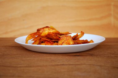 Kurutulmuş ve kızarmış kaju dilimleri ile baharatlı biber sosu karıştırılmış beyaz tabakta ahşap dokuda izole edilmiş. Bu yerel Malezya geleneksel abur cuburu Kerepek Ubi olarak da bilinir.. 