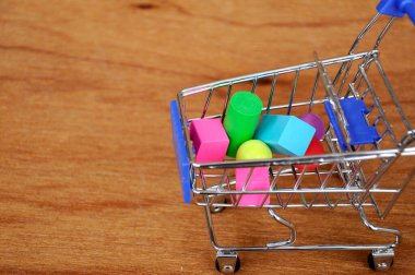 Oyuncak alışveriş vagonunun içindeki tahta desenli plastik küp ve diğer şekillerle dolu.. 