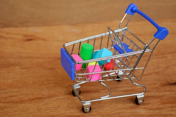 Oyuncak alışveriş vagonunun içindeki tahta desenli plastik küp ve diğer şekillerle dolu.. 