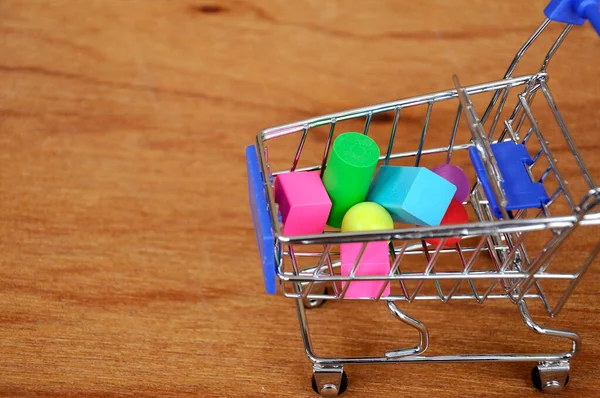 Oyuncak alışveriş vagonunun içindeki tahta desenli plastik küp ve diğer şekillerle dolu.. 