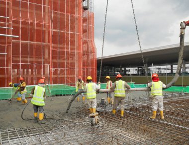 SELANGOR, MALAYSIA -13 Temmuz 2016: İnşaat alanındaki inşaat sahasının zeminine beton kova döken bir grup inşaat işçisi.  