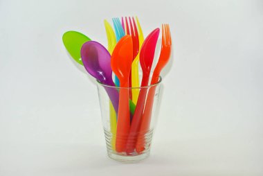 Renkli plastik kaşıklar ve çatallar beyaz arka planda cam bardakta