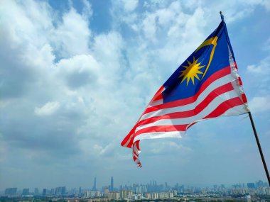 KUALA LUMPUR, MALAYSIA - 1 Temmuz 2022: Malezya bayrağı Jalur Gemilang yüksek bir yerde ve Kuala Lumpur siluetinin zemininde dalgalanır