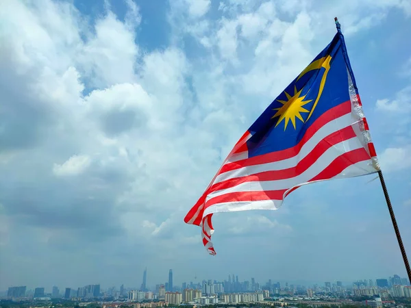 KUALA LUMPUR, MALAYSIA - 1 Temmuz 2022: Malezya bayrağı Jalur Gemilang yüksek bir yerde ve Kuala Lumpur siluetinin zemininde dalgalanır
