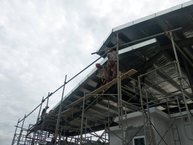 SELANGOR, MALAYSIA -JUNE 16, 2021: Construction workers install trusses and roofing sheets at construction sites. Lightweight roof trusses used are more economical, sturdy and fast.