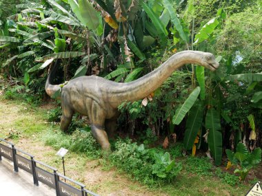 MELAKA, MALAYSIA - JUNE 6, 2022: Replicas of various types of dinosaurs built to life size. It is decorated with tropical plants to make it seem alive.