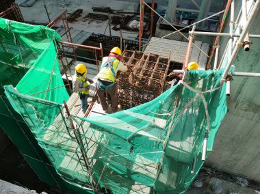 KLANG, MALAYSIA -MARCH 31, 2022: Construction workers fabricating steel reinforcement bar at the construction site. They tied it together using the tiny wires. It is part of reinforcement concrete.