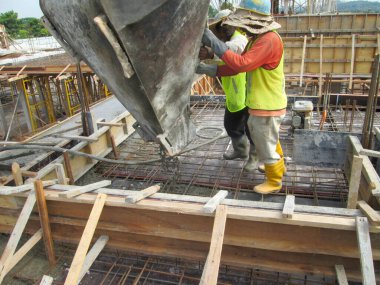 JOHOR, MALAYSIA -JANUARY 16. 2017: Group of construction workers pouring wet concrete using concrete bucket into the timber form work at the construction site.  