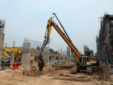 SELANGOR, MALAYSIA 15 Mart 2016: İnşaat alanında çarşaf yığını cofferdam sürücü makine. Makine titreşimli hidrolik kol kullanarak çarşaf yığınını yere itti. İşçi kontrolü. 