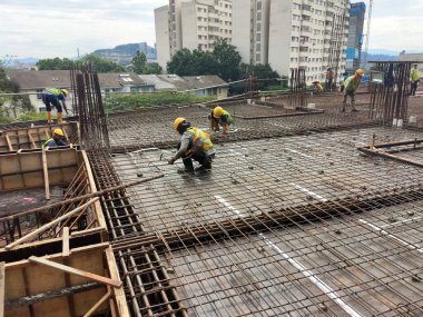 MELAKA, MALAYSIA - 1 Temmuz 2022: İnşaat işçileri yer döşemeleri için çelik takviye çubukları üretiyorlar. Çeşit büyüklükteki inşaat demiri mühendis tarafından dizayn edilip bağlanır..