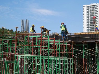 MELAKA, MALAYSIA - 5 Haziran 2022: İnşaat işçileri güvenliklerinden emin olmak için yükseklerde çalışır ve güvenlik teçhizatı giyerler. Gruplar halinde çalışır ve görevlerini yerine getirirler..