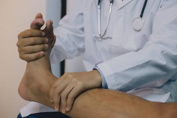 Крупный план физиотерапевта, выполняющего упражнения на ступне человека. Он использовал ручку для ног пациента, чтобы проверить боль.