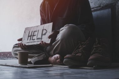 Evsiz, yetişkin bir adam binanın gölgesinde oturmuş yardım ve para dileniyor. Evsiz konsepti