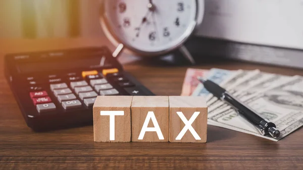 Debt collection and tax season concept. The word tax written in wooden block letters with calculator, money, clock, pen, background, Time to pay concept