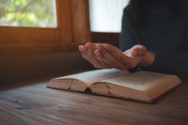 Yakın plan Hıristiyan kadınlar İncil okur. Elleri katlanmış, kutsal bir İncil 'in üzerinde, ahşap bir masanın üzerinde.