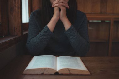 Yakın plan Hıristiyan kadınlar İncil okur. Elleri katlanmış, kutsal bir İncil 'in üzerinde, ahşap bir masanın üzerinde.