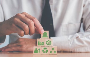 Elle istiflenmiş tahta bloklar masaya basar ve güzel beyaz arkaplanda ESG simgesiyle çevrelenmiş 
