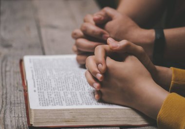 Yakın plan iki Hıristiyan İncil okuyor. Ellerin, kutsal bir İncil 'in üzerinde, ahşap bir masanın üzerinde dua ederken bükülmüş. Çevrimiçi grup ibadeti, Dünya Dua Günü, Uluslararası Dua Günü, Umut, Minnet, Müteşekkir, Güven