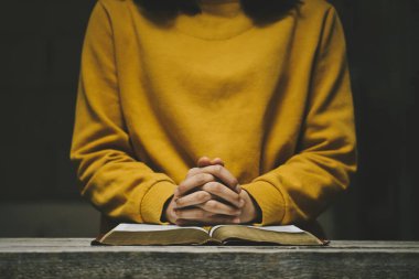 Sabahları kutsal İncil 'in üzerinde dua eden bir kadın. Tahta bir masada el ele dua etmek. Hristiyan hayatı, Tanrı 'ya dua etmek. Kilisenin inanç kavramında kutsal bir İncil üzerine dua ederken eller katlandı..