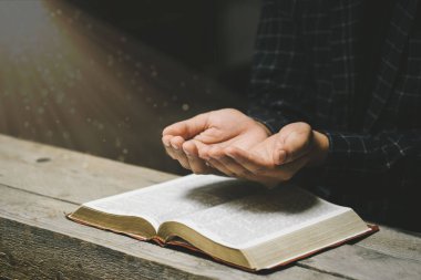 İnsan elleri İncil 'le Tanrı' ya dua ediyor. Sarı ışıklar ve parıltılar geliyor. İyiliğe inan. Tahta bir masada el ele dua etmek. Umudun, sevginin ve bağlılığın gücü. 