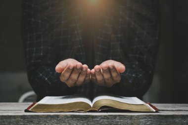 İnsan elleri İncil 'le Tanrı' ya dua ediyor. Sarı ışıklar ve parıltılar geliyor. İyiliğe inan. Tahta bir masada el ele dua etmek. Umudun, sevginin ve bağlılığın gücü. 